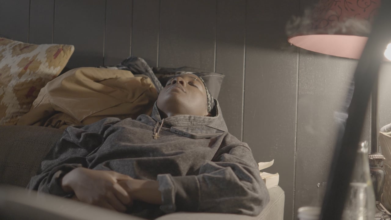 A figure asleep on a couch under lamplight